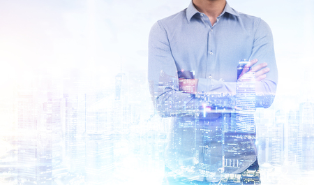 Close up of a businessman in a blue shirt standing against a blue city panorama. Mock up. Toned image. Double exposureの写真素材