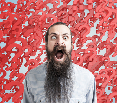 Screaming bearded man stressed because of numerous questions. Abstract red questionmark background. Obsessive compulsive anxiety disordersの写真素材
