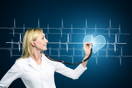 Attractive smiling female doctor checking heart beat. Healthy heartbeat chart. Medicine and health conceptの写真素材