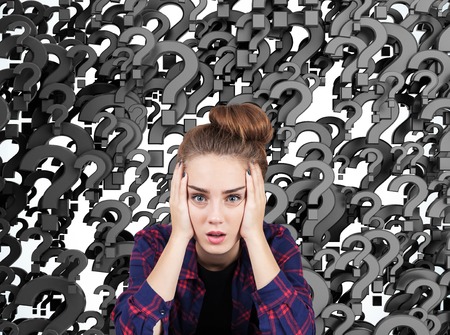 Portrait of a stressed out teen girl sitting against black question marks background. Concept of multiple questions that need to be answered.の写真素材