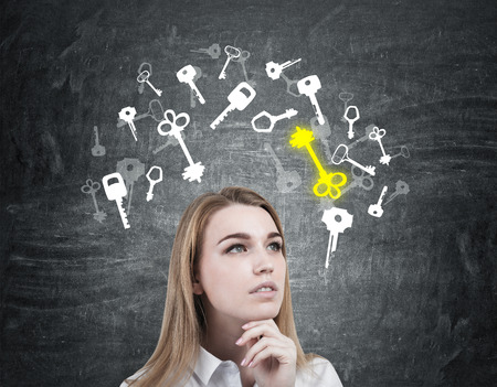 Portrait of a pensive blond womans head. She is standing near a blackboard with yellow and white key sketches drawn on it.の写真素材