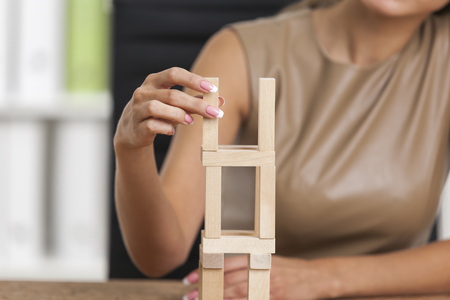 Businesswoman in beige is playing with wooden bricks at her workplace in a white office. Concept of a breakの写真素材