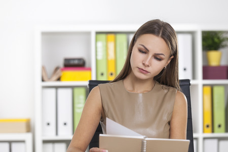 Portrait of a centered woman with blond hair wearing beige clothes. She is at her workplace reading a notebook.の写真素材