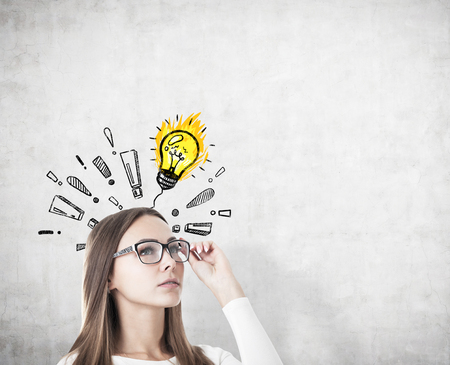 Portrait of a serious businesswoman in glasses standing near a concrete wall with a light bulb sketch surrounded by exclamation marks. Mock up.の写真素材