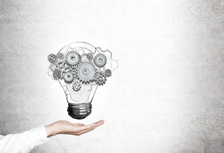 Close up of a hand of a woman with a light bulb sketch hovering above it. There are cogs and gears in it. Mock up.の写真素材