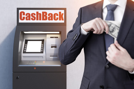 Close up of a businessman wearing a black suit who has taken money from a black atm machine. He is puting it in the pocket.の写真素材