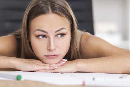 Close up of a young designer with blond hair looking at the viewer while she laid her head on her hands. There are markers in the foreground.の写真素材