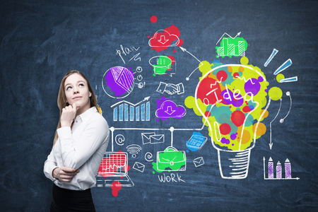 Portrait of a blond businesswoman wearing a white shirt and standing near a blackboard with a colorful creative idea sketch.の写真素材
