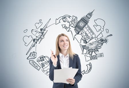 Portrait of a blond woman with a stack of documents standing near a gray wall with sights drawings depicted on it.の写真素材