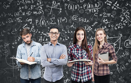 Portrait of a young business team standing with books and a tablet computer near a blackboard with formulas on it. Concept of a startup and business education.の写真素材