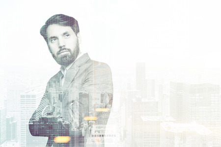 Portrait of a serious bearded businessman standing with crossed arms against a gray city panorama. Double exposure. Mock up. Toned imageの写真素材
