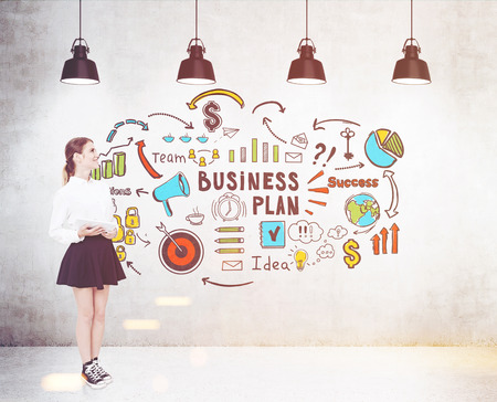 Side view of a girl wearing sneakers and standing near a concrete wall with a colorful business plan drawing on it. Toned imageの写真素材