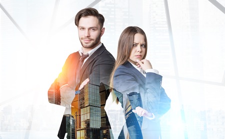 Close up of a bearded businessman and a pensive businesswoman standing in an office near a large gray skyscraper panorama in the morning. Toned image. Mock up. Double exposureの写真素材