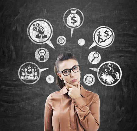 Portrait of a pensive businesswoman in brown standing near a blackboard with money icons drawn on it.の写真素材