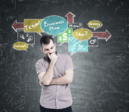 Portrait of a pensive bearded businessman in a pink shirt standing near a chalkboard with colorful speech bubbles on it.の写真素材