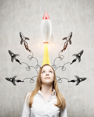 Portrait of a blond businesswoman standing near a concrete wall with many rockets taking off above her head.の写真素材
