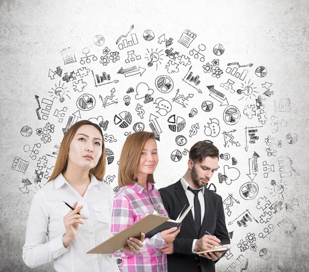 Portrait of two businesswomen and a businessman standing near a concrete wall with a business sketch drawn on it.の写真素材