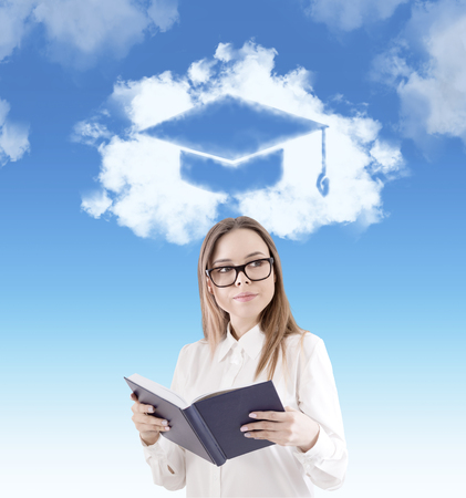 Portrait of a nerd girl wearing glasses and holding a book. There is a graduation hat sketch in the sky above her head.の写真素材