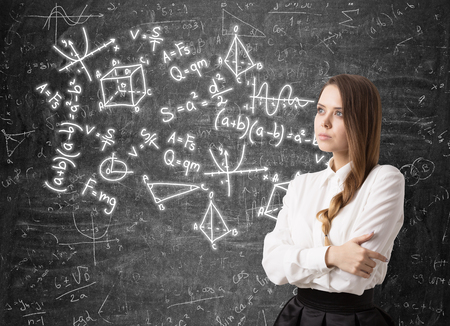Portrait of a serious woman with braided hair standing with crossed arms near a blackboard with math formulas written on it.の写真素材