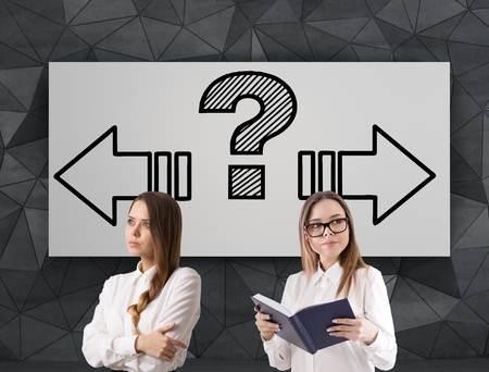Portrait of two young women standing near a choice poster with to arrows pointing in different directions. Concept of decision making.の写真素材
