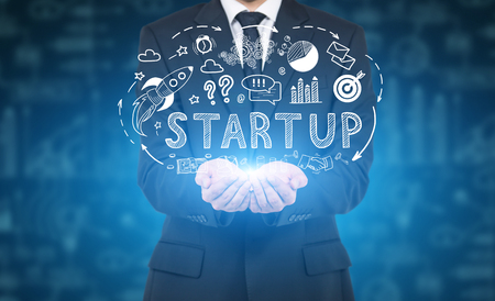 Close up of a businessman wearing a suit and a tie and interacting with a start up hologram near a blue wall.の写真素材