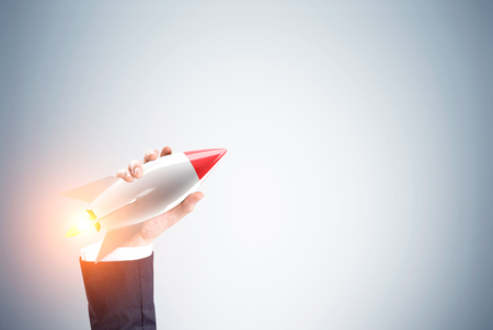 Close up of a hand of a businessman holding a toy rocket against a gray wall. Toned image. Mock upの写真素材