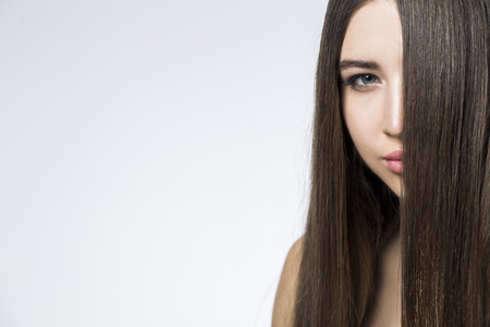 Close up of a suspecting young woman with long brown hair covering half of her face. She is looking at you. Mock upの写真素材