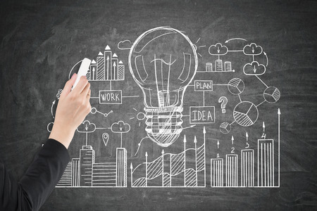 Close up of a hand of a businesswoman wearing a black suit drawing a business idea sketch on a blackboard.の写真素材
