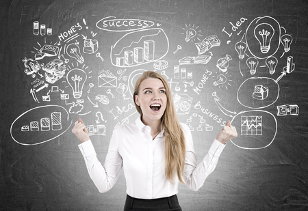 Portrait of a happy woman screaming with joy while standing near a blackboard with a business scheme sketch on it.の写真素材