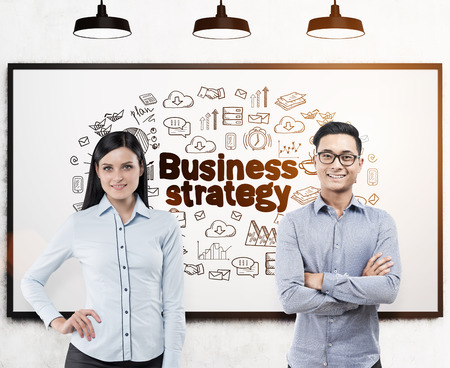 Portrait of an Asian businessman and his colleague in a blue shirt standing near a whiteboard with a business strategy sketch drawn on it. Toned imageの写真素材
