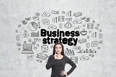 Portrait of a pensive woman in a dress standing near a concrete wall with a business strategy sketch drawn on it.の写真素材