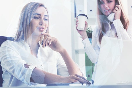Businesswoman is working at her laptop in an office while her colleague is talking on the phone and holding a coffee to go. Toned image, film effectの写真素材