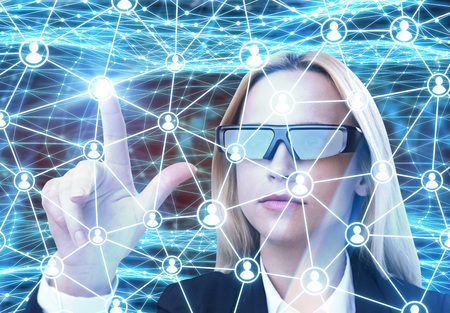 Close up of a blond businesswoman in augmented reality glasses interacting with a network hologram. Abstract blue backgroundの写真素材