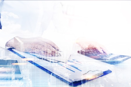 Close up of woman s hand with a calculator. She is holding a pen ready to take notes in her notebook. Cityscape. Toned image double exposureの写真素材
