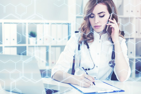 Portrait of a woman doctor with red hair talking on the phone in her office and taking notes in a...