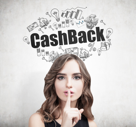Close up of a young European woman with wavy hair making a hush sign. Concrete wall background with a cashback sketch on it.の写真素材