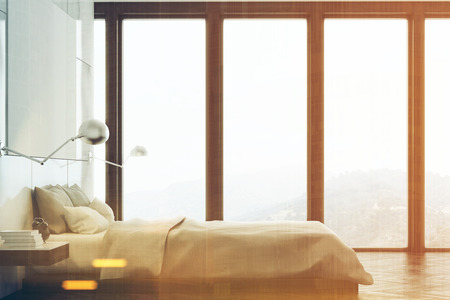 Marble bedroom interior with a panoramic window, a bed standing along it and a large horizontal poster hanging above. A home office is in the background. Front view. 3d rendering mock up toned imageの写真素材