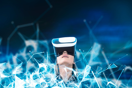 Portrait of a young woman wearing VR glasses and looking upwards. An abstract blue pattern against a...