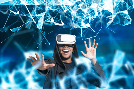 Portrait of an excited African American man wearing a hoodie and VR glasses. He is interacting with a abstract glowing blue linesの写真素材