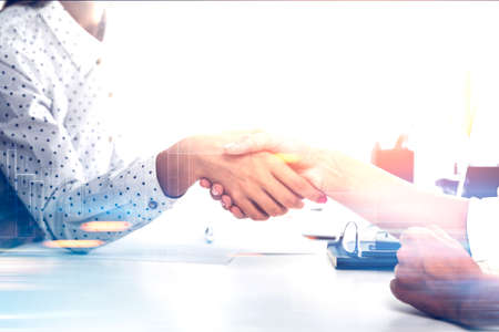 Close up of two women in a white office. They are seating at a table and shaking hands. Negotiations. Toned image double exposureの写真素材
