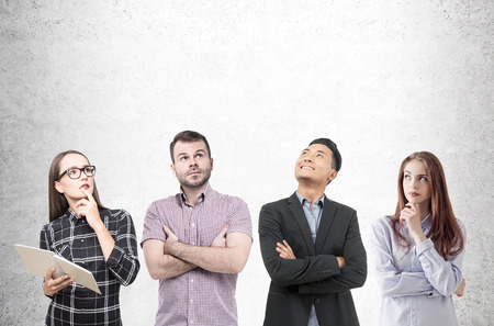 Two women and two men are standing together near a concrete wall. One of them is holding an open book. Brainstorming. Mock upの写真素材