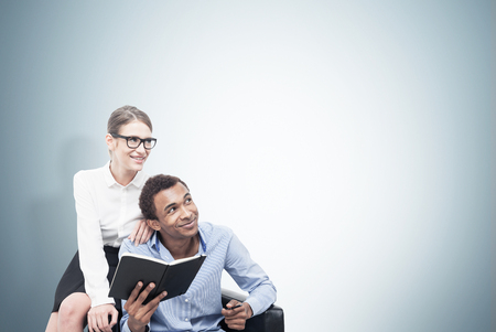 Portrait of a smiling African American man wearing a blue shirt and a young blond woman wearing glasses and sitting on a leather armchair near him. Mock upの写真素材