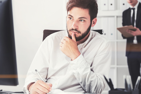 Portrait of a serious black haired young businessman looking at his computer screen and taking notes. Concept of planning. Toned imageの写真素材