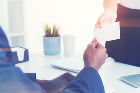 Close up of an unrecognizable young woman giving her business card to an African American businessman sitting with his back to the camera. Concept of business contacts. Mock upのeditorial素材