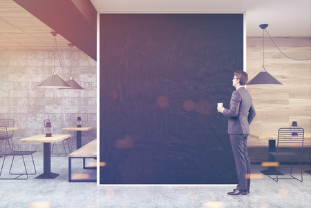 Man in a wooden and dark gray wall cafe interior with a large black wall fragment in the center and old oil lamps on square wooden tables. 3d rendering mock up toned imageの写真素材