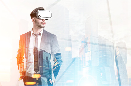 Front view of a bearded man wearing a suit and VR glasses and standing against a modern foggy...