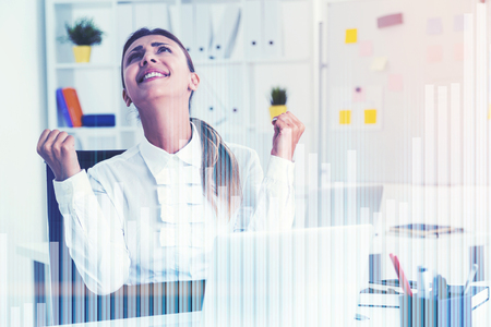 Close up portrait of a black haired businesswoman wearing a white shirt and sitting at her table in a white office. Graphs in the foreground. Toned image double exposureの写真素材