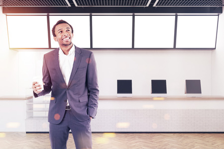 African American man in a modern cafe interior with tablet computers standing on a wooden and marble counter. Black ceiling. 3d rendering mock up toned imageの写真素材
