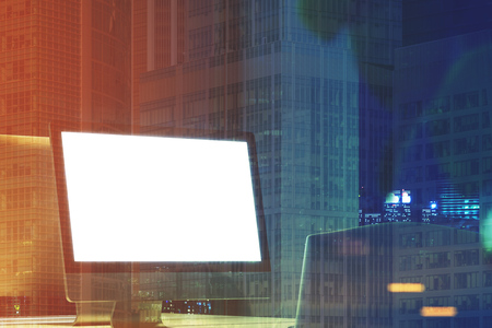 Close up of a blank computer screen standing on a desk in a night office with large windows. There...