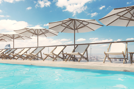 White deck chairs are standing under beach umbrellas near a swimming pool. A blue sky with clouds is above them. Side view. 3d rendering mock upの写真素材